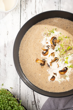 A mushroom soup with thyme, sour cream and fried mushrooms in a deep black bowl on a white wooden table, top viewの写真素材