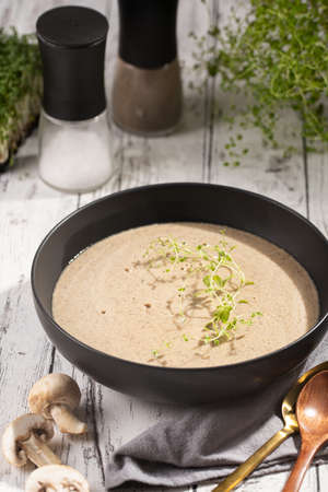 A champignon mushroom soup with thyme in a deep black bowl on a white wooden tableの写真素材