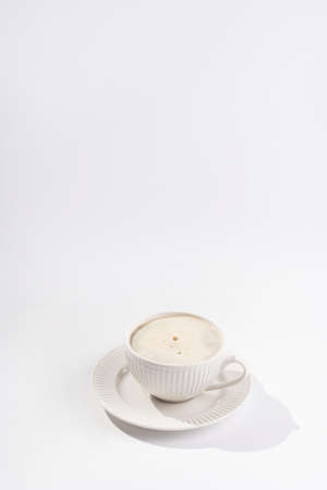 A white porcelain cup with coffee drink cappuccino on a white saucer plate on a white surfaceの写真素材