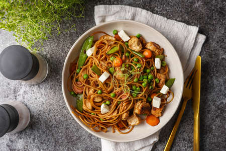 Italian pasta spaghetti with chicken, green beans and cheese mozzarella and fresh thyme in light gray bowl on gray concrete surface, golden silverware and beige colored napkin, top viewの写真素材