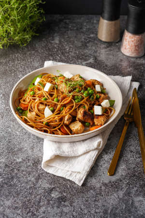 Italian pasta spaghetti with chicken, green beans and cheese mozzarella and fresh thyme in light gray bowl on gray concrete surface, golden silverware and beige colored napkinの写真素材