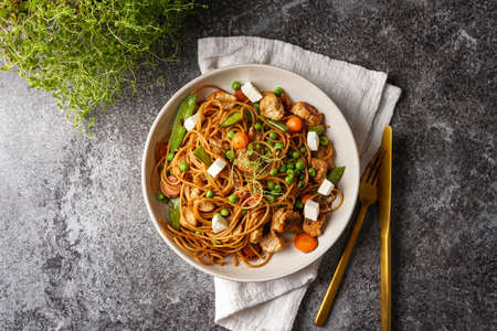 Italian pasta spaghetti with chicken, green beans and cheese mozzarella and fresh thyme in light gray bowl on gray concrete surface, golden silverware and beige colored napkin, top viewの写真素材