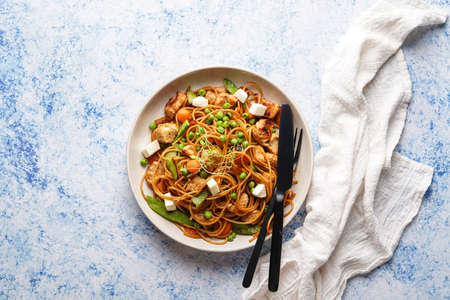 Italian pasta spaghetti with chicken, green beans and cheese mozzarella and fresh thyme in light gray bowl on blue surface, black silverware and beige colored napkin, top viewの写真素材