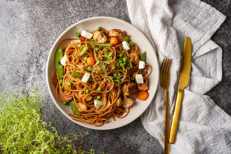 Italian pasta spaghetti with chicken, green beans and cheese mozzarella and fresh thyme in light gray bowl on gray concrete surface, golden silverware and beige colored napkin, top viewの写真素材