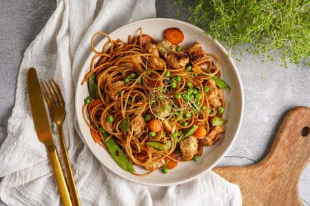 Italian pasta spaghetti with chicken, green beans and cheese mozzarella and fresh thyme in light gray bowl on gray concrete surface, golden silverware and beige colored napkin, top viewの写真素材