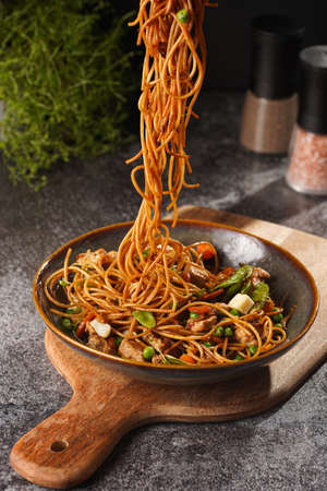 Female hand holding a fork with Italian pasta spaghetti with chicken, green beans, cheese mozzarella and fresh thyme in green bowl on wooden board on gray concrete surfaceの写真素材