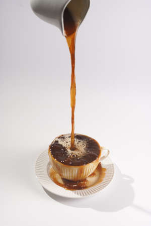 Pouring coffee into a white porcelain cup with coffee drink cappuccino on a white saucer plate on a...