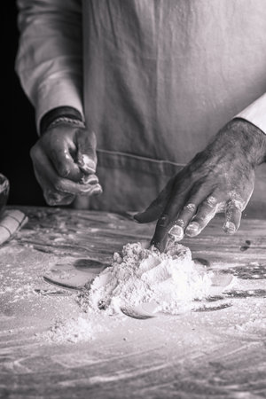 A male chef cook in a white shirt and gray apron making dough out of flour, black and white
