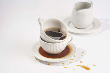a white porcelain cup with cappuccino stacked in another mug on a white saucer plate on a white surfaceの写真素材