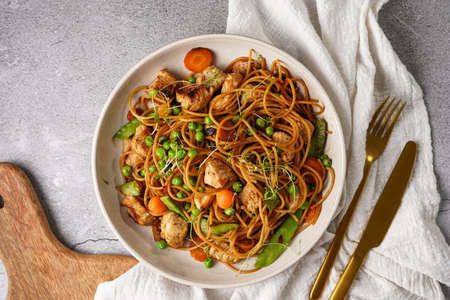 Italian pasta spaghetti with chicken, green beans and cheese mozzarella and fresh thyme in light gray bowl on gray concrete surface, gold silverware and beige colored napkinの写真素材