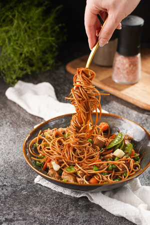 Female hand holding a fork with Italian pasta spaghetti with chicken, green beans, cheese mozzarella and fresh thyme in green bowl on wooden board on gray concrete surfaceの写真素材