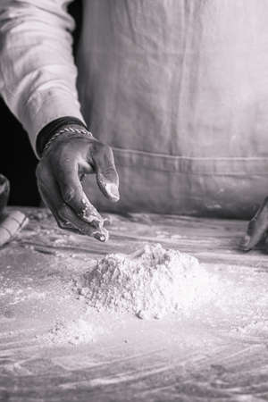 A male chef baker in a white shirt and gray apron making dough on a dark kitchen table, black and whiteの写真素材