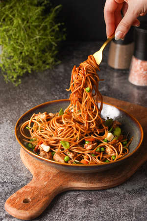 Female hand holding a fork with Italian pasta spaghetti with chicken, green beans, cheese mozzarella and fresh thyme in green bowl on wooden board on gray concrete surfaceの写真素材