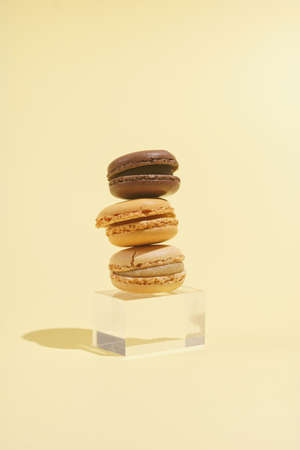 Three creamy and chocolate macaron pastry stacked on top of each other - hard light on beige colored surfaceの写真素材