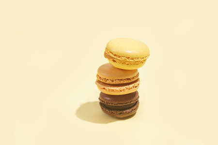 Three creamy and chocolate macaron pastry stacked on top of each other - hard light on beige colored surfaceの写真素材