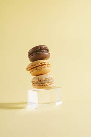 Three creamy and chocolate macaron pastry stacked on top of each other - hard light on beige colored surfaceの写真素材