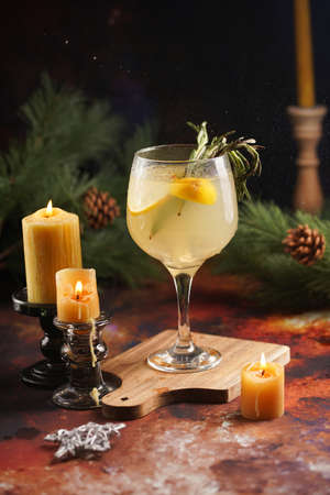 A big glass with christmas drink lemonade with rosemary and lemons surrounded by christmas decoration, lights and candlesの写真素材