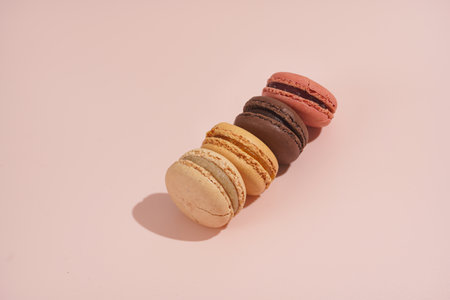 Several creamy, pink and chocolate macaron pastry stacked on top of each other - hard light on beige colored surfaceの写真素材