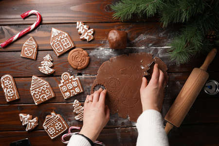 Gingerbread cookies with white sugar frosting shaped like houses and chocolate honey dough rolled on a wooden table surrounded by Christmas decorationの写真素材