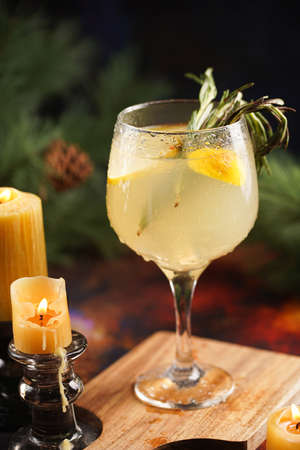 A big glass with christmas drink lemonade with rosemary and lemons surrounded by christmas decoration, lights and candlesの写真素材