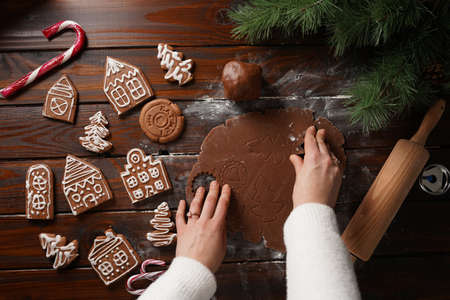 Gingerbread cookies with white sugar frosting shaped like houses and chocolate honey dough rolled on a wooden table surrounded by Christmas decorationの写真素材