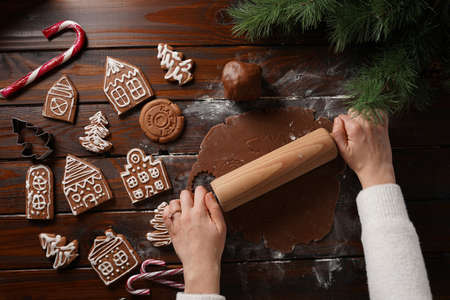 Gingerbread cookies with white sugar frosting shaped like houses and chocolate honey dough rolled on a wooden table surrounded by Christmas decorationの写真素材