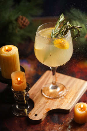 A big glass with christmas drink lemonade with rosemary and lemons surrounded by christmas decoration, lights and candlesの写真素材