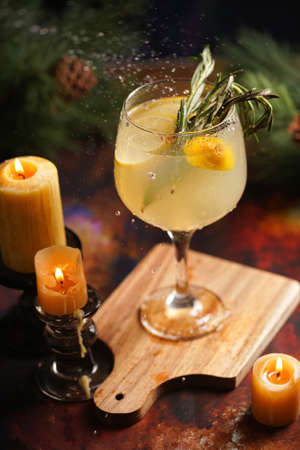 A big glass with christmas drink lemonade with rosemary and lemons surrounded by christmas decoration, lights and candlesの写真素材