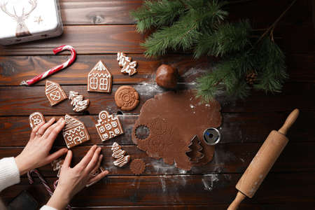 Gingerbread cookies with white sugar frosting shaped like houses and chocolate honey dough rolled on a wooden table surrounded by Christmas decorationの写真素材