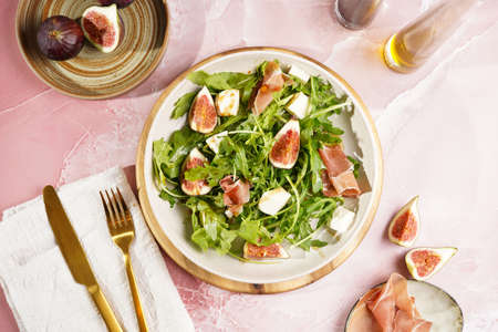 A beige colored plate with arugula salad with mozzarella, figs and pork meat jamon and balsamico dressing on a pink marble surface, top viewの写真素材