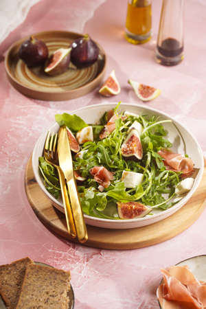 A beige colored plate with arugula salad with mozzarella, figs and pork meat jamon and balsamico dressing on a pink marble surfaceの写真素材