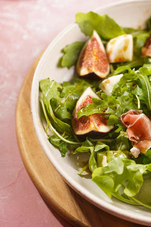 A beige colored plate with arugula salad with mozzarella, figs and pork meat jamon and balsamico...