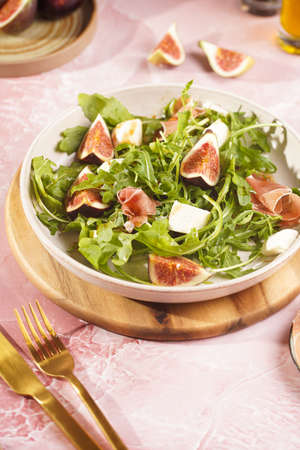 A beige colored plate with arugula salad with mozzarella, figs and pork meat jamon and balsamico dressing on a pink marble surfaceの写真素材