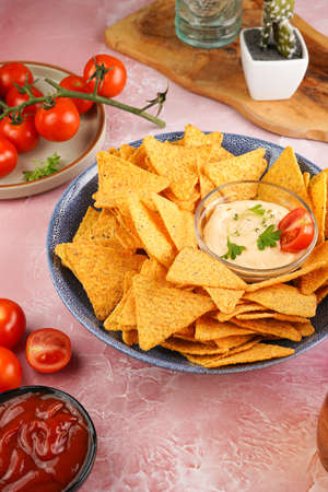 A blue bowl with cheese tortilla chips and a chilli cheese dip on a pink marble surface, cherry tomatoes, ketchupの写真素材