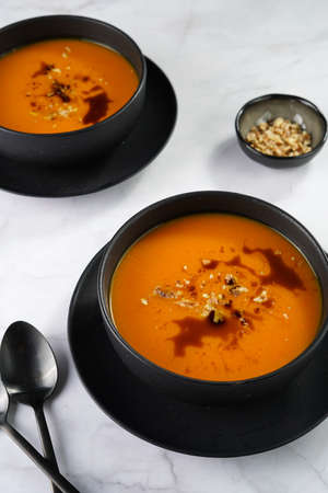 Two deep black bowls with an orange pumpkin cream soup with pumpkin seed oil, two black spoons on a marble surfaceの写真素材