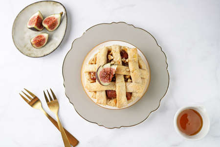 A sweet fig tart pastry on a sophisticated plate, two golden dessert spoons, honey, cut figs on a...
