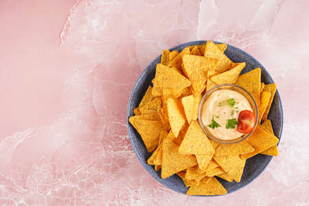 A blue bowl with cheese tortilla chips and a chilli cheese dip on a pink marble surface, top viewの写真素材