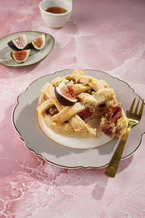 A sweet fig tart pastry on a sophisticated plate, two golden dessert spoons, honey, cut figs on a marble surfaceの写真素材