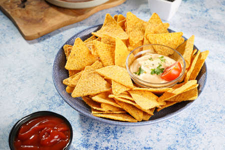 A blue bowl with cheese tortilla chips and a chilli cheese dip on a blue marble surfaceの写真素材