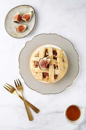 A sweet fig tart pastry on a sophisticated plate, two golden dessert spoons, honey, cut figs on a marble surface, top viewの写真素材