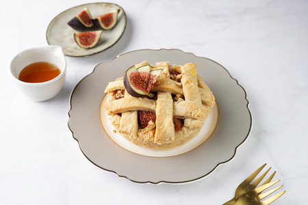 A sweet fig tart pastry on a sophisticated plate, two golden dessert spoons, honey, cut figs on a marble surfaceの写真素材