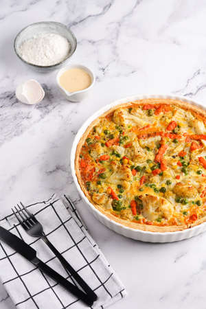 Baked french vegetable pie quiche filled with carrots, peas and cheese on a marble surface, cracked egg shell, flour, creamの写真素材