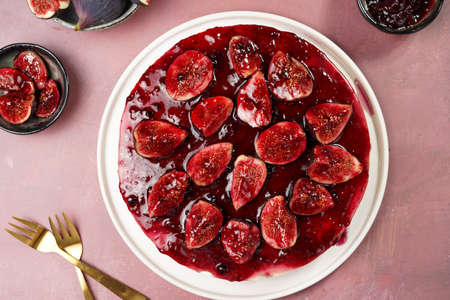 A red cake on a white plate on a burgundy surface: no bake cheesecake with dark red jelly and fig slices, top viewの写真素材