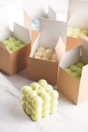 Green, blue and white square bubble candles on a marble surface in craft paper boxesの写真素材