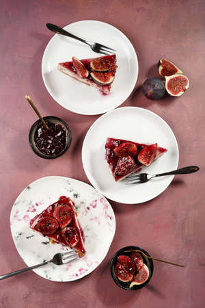 Several pieces of cake on a white plate on a burgundy surface: no bake cheesecake with dark red jelly and fig slices, top viewの写真素材