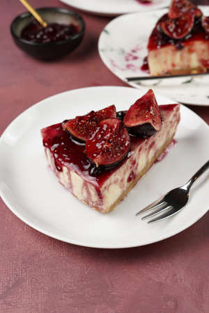 A piece of cake on a white plate on a burgundy surface: no bake cheesecake with dark red jelly and fig slicesの写真素材