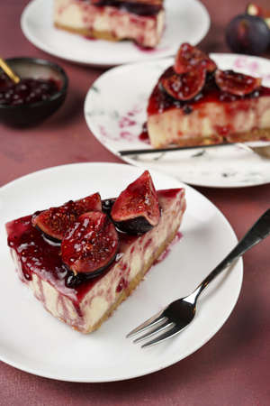 A piece of cake on a white plate on a burgundy surface: no bake cheesecake with dark red jelly and fig slicesの写真素材