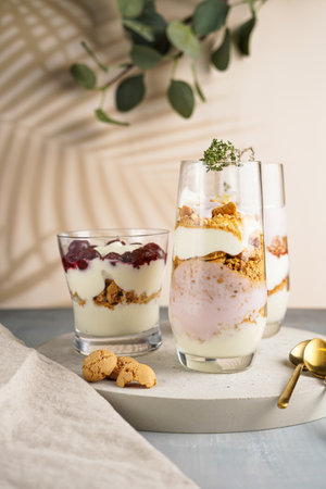 Three glasses with a layered creamy yoghurt dessert trifle with cookies, amaretti and cherries in a tropical settingの写真素材