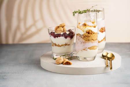 Three glasses with a layered creamy yoghurt dessert trifle with cookies, amaretti, cherries and thyme in a tropical settingの写真素材