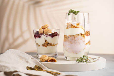 Three glasses with a layered creamy yoghurt dessert trifle with cookies, amaretti, cherries and thyme in a tropical settingの写真素材